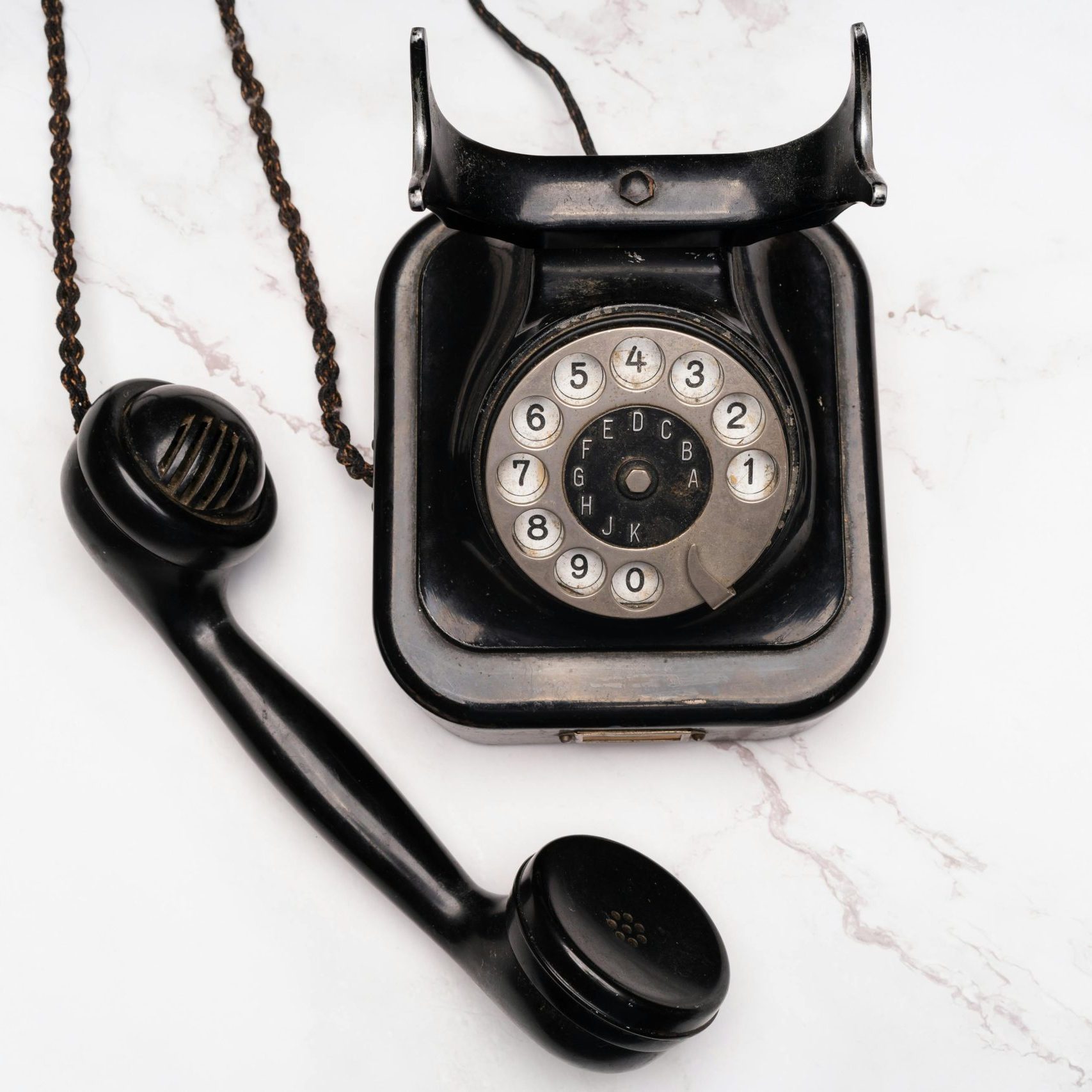 Old-fashioned rotary dial telephone with receiver on white marble background.