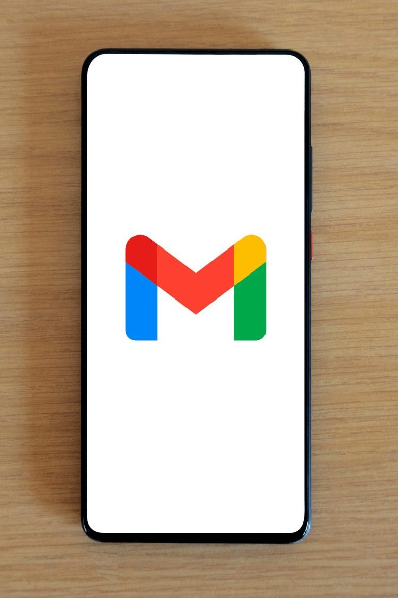 A smartphone displaying the Gmail app logo on a wooden surface, viewed from above.